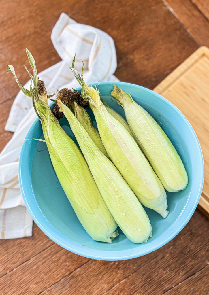 Corn cobs in the husk in a blue bowl.