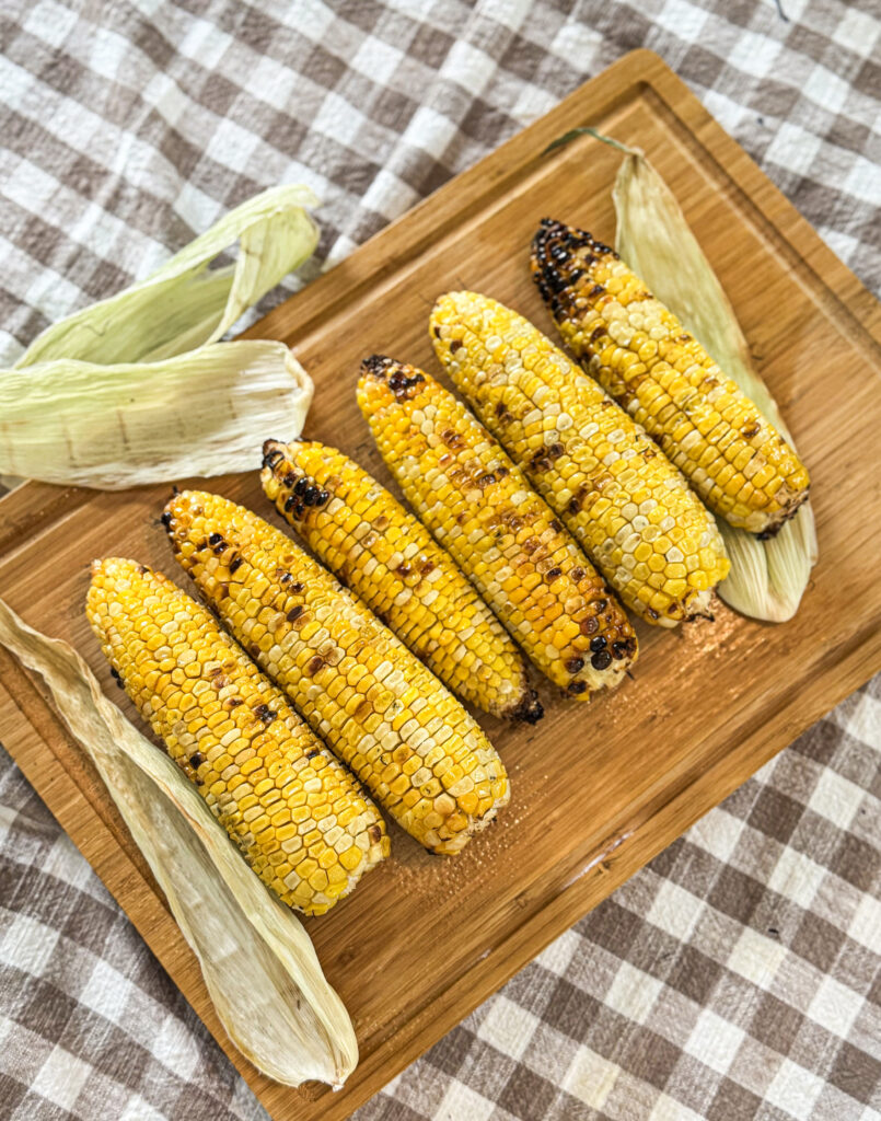 Delicious grilled corn on the cob over a wooden cutting board on a checkered table cloth