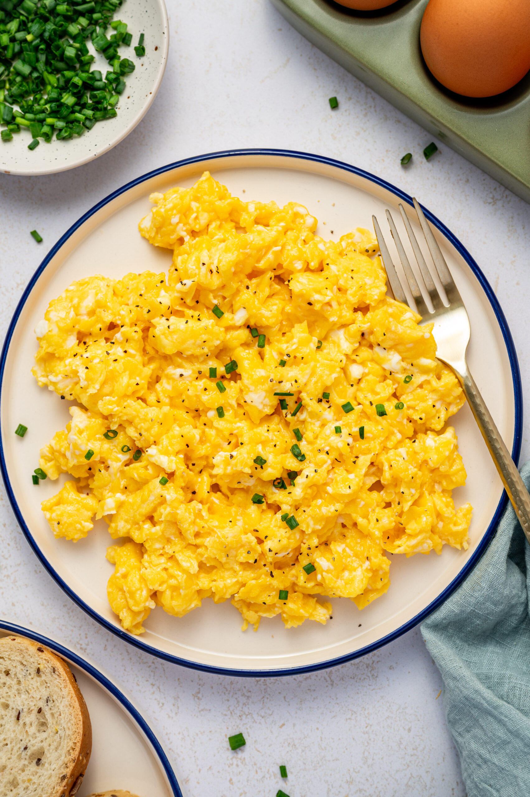 Restaurant-style scrambled eggs on a white plate with chives as garnish.