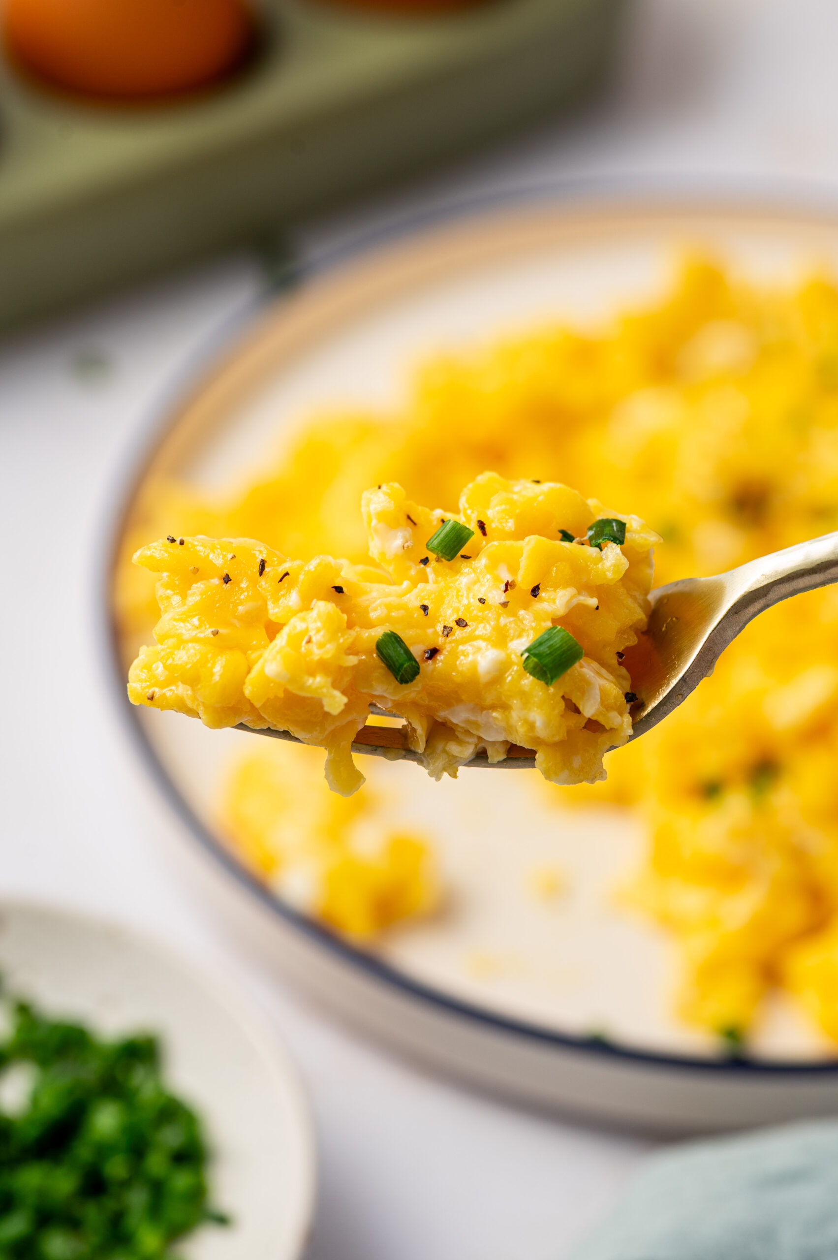 A forkful of restaurant-style scrambled eggs hovering over a plate.