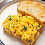 Restaurant-style scrambled eggs on toast with chives as garnish.