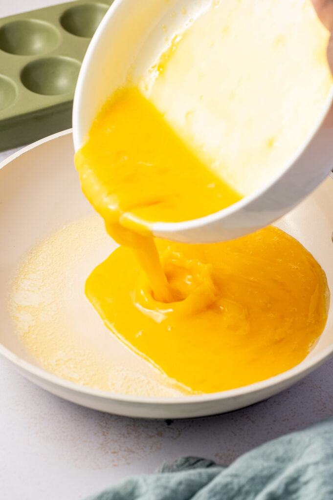 Pouring whisked eggs into a white skillet.