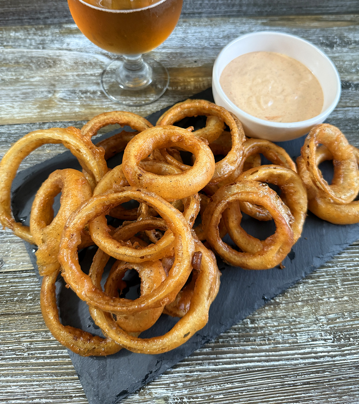 A plate of beer battered onion rings with dipping sauce.
