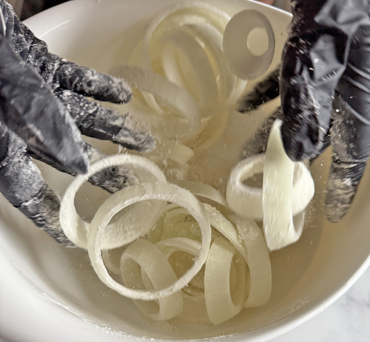 Dusting onion rings with flour to make beer-battered onion rings.