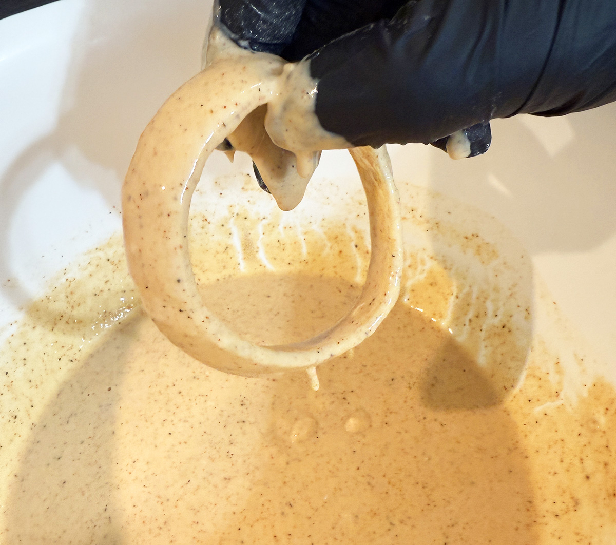Dipping raw onion rings into beer batter.