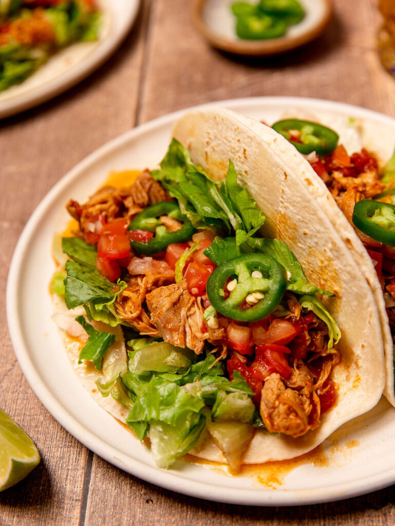 Close-up of an Instant Pot chicken taco on white plate with toppings.
