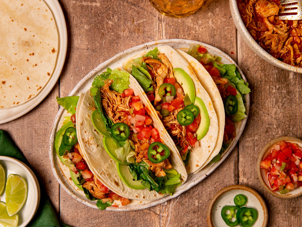 Loaded Instant Pot chicken tacos on a serving plate over a wooden surface.