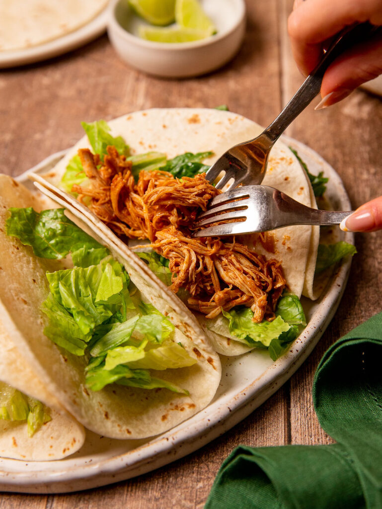 Adding pulled chicken to a tortilla with lettuce.