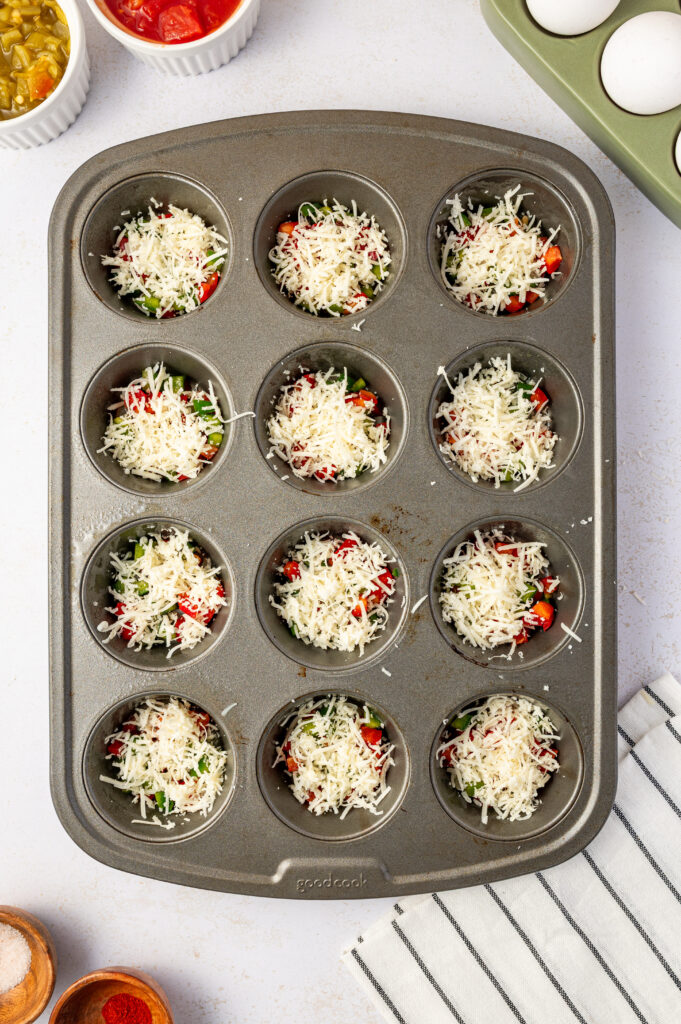 Peppers, tomatoes, green chilies, and shredded cheese in a muffin tin.