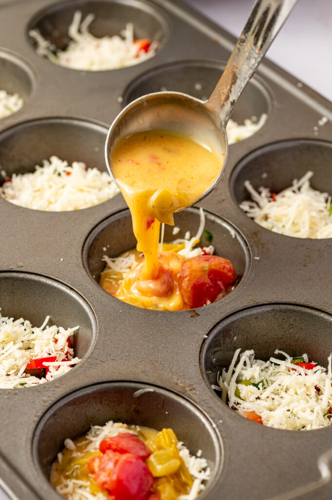 Filling a muffin tin with Southwest scrambled egg bites with tomatoes, peppers, and green chilies.