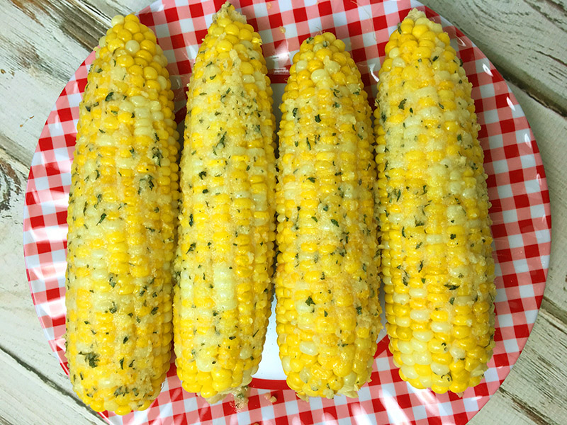 A plate full of corn on the cob seasoned with ranch seasonings and Parmesan cheese.