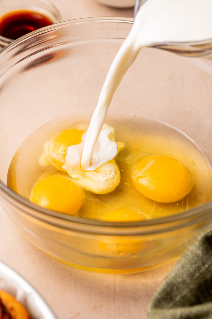 Pouring milk in a glass bowl with eggs.