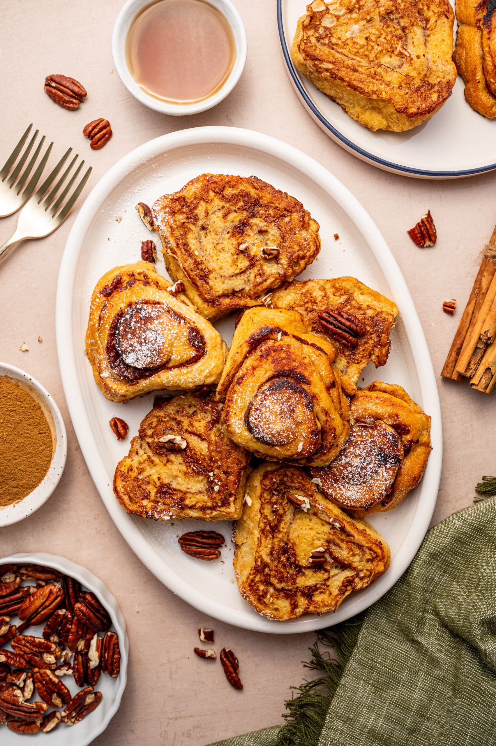 A white serving plate of cinnamon roll French toast with maple syrup and pecans.