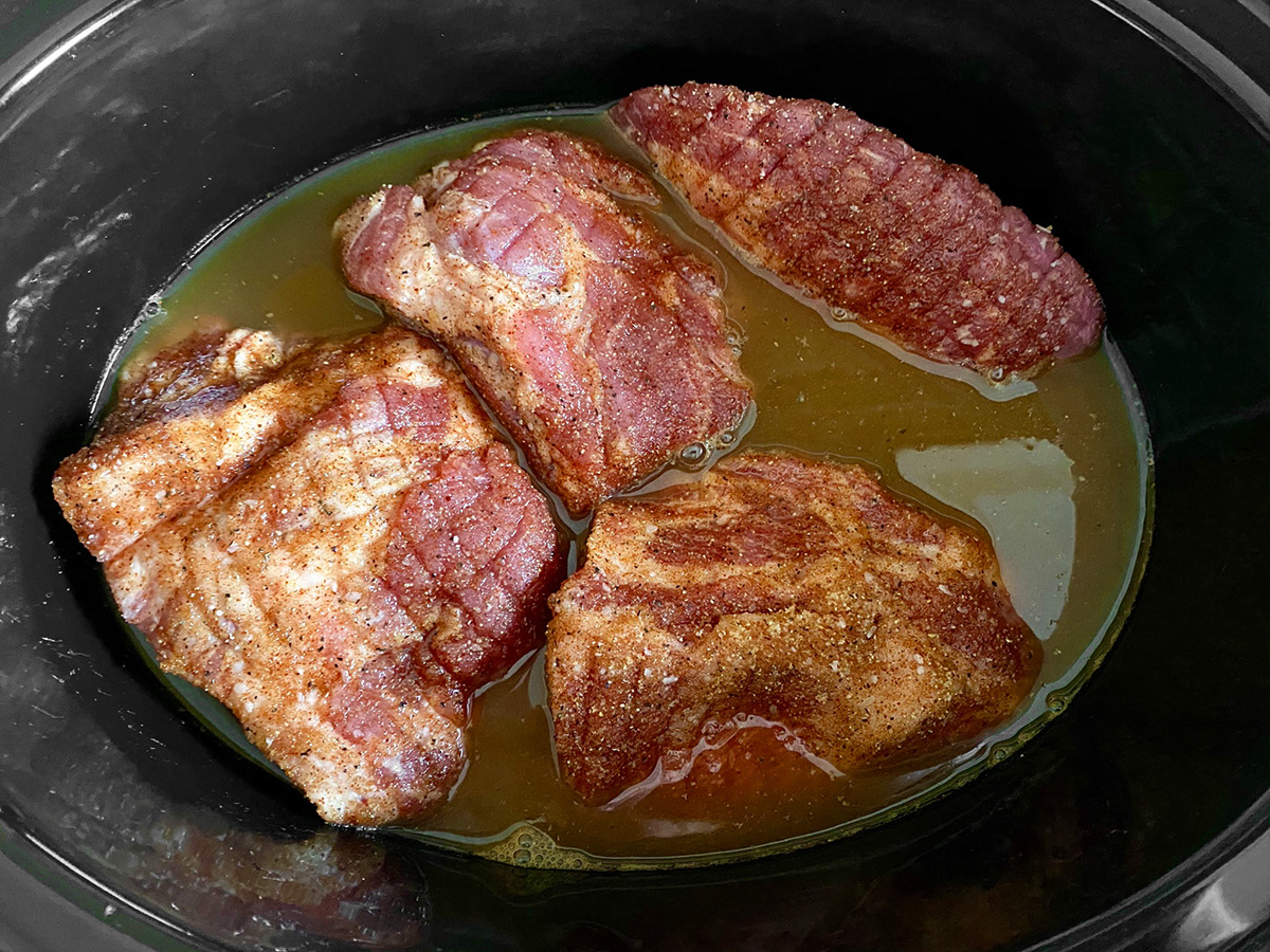 Seasoned pork chunks with liquid in a slow cooker.