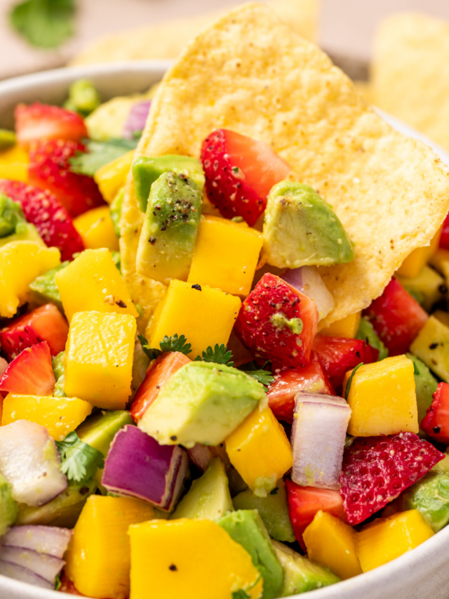 A tortilla chip dipped into chunky mango salsa.