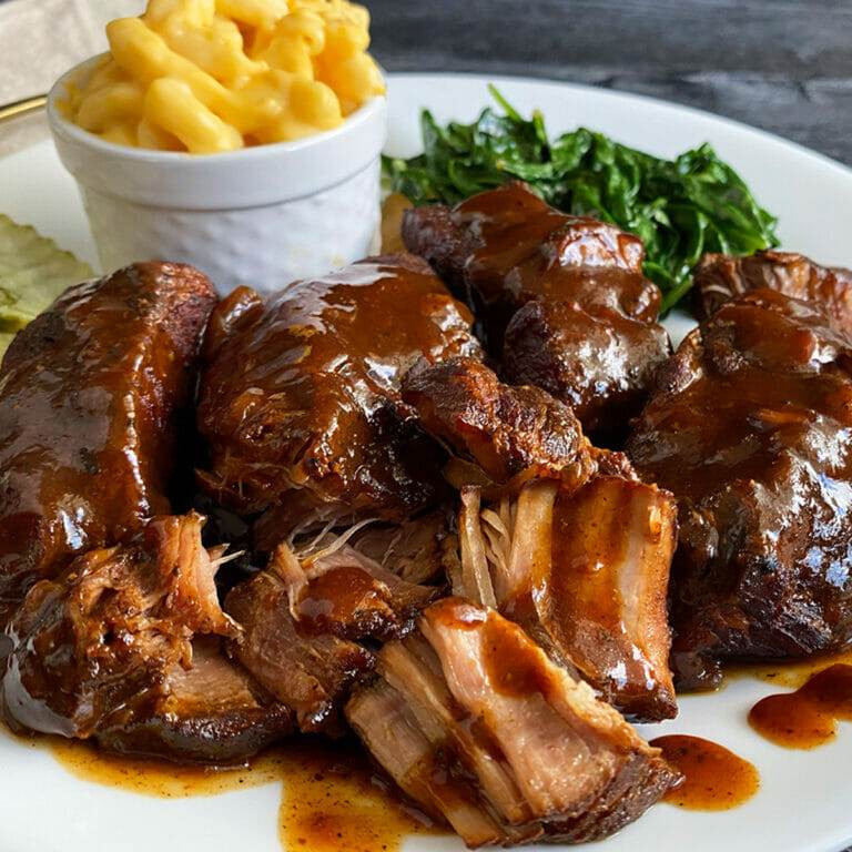 A plate of BBQ country style ribs, made in an Instant Pot, served with mac and cheese and garlic spinach.