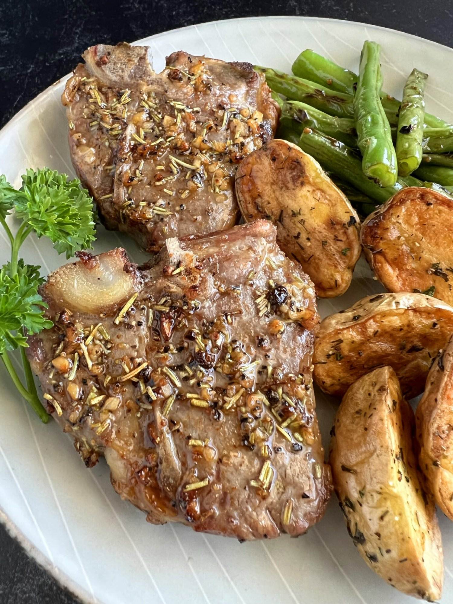 Air fryer Lamb chops on a white plate with a side of roasted potatoes and green beans.