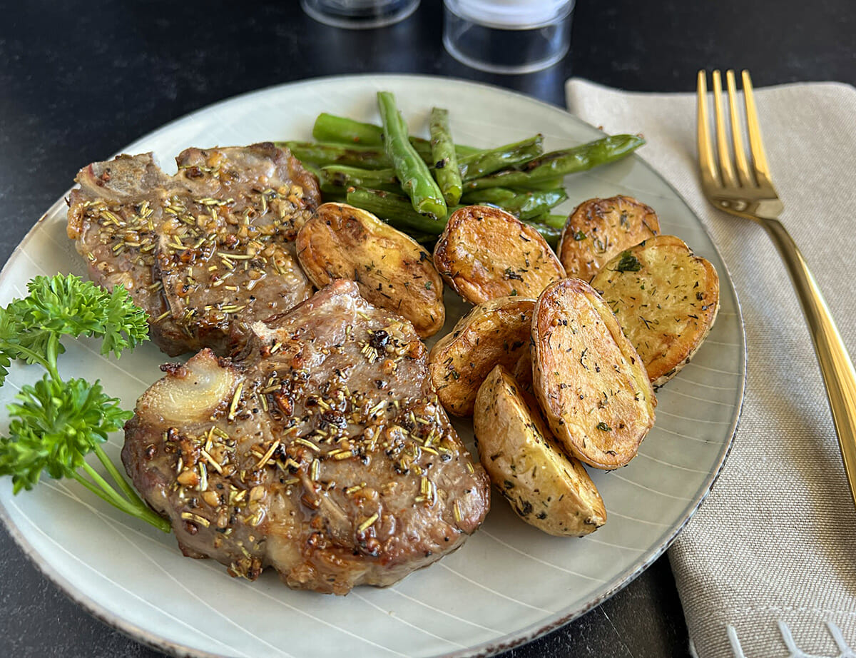 a plate of air fryer lamb chops served with roasted potatoes and sauteed green beans