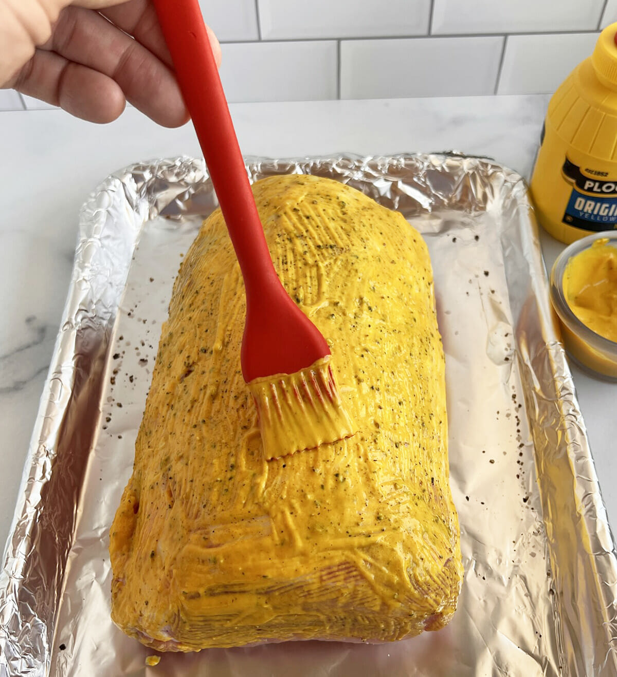 Brushing mustard onto a pork loin roast.