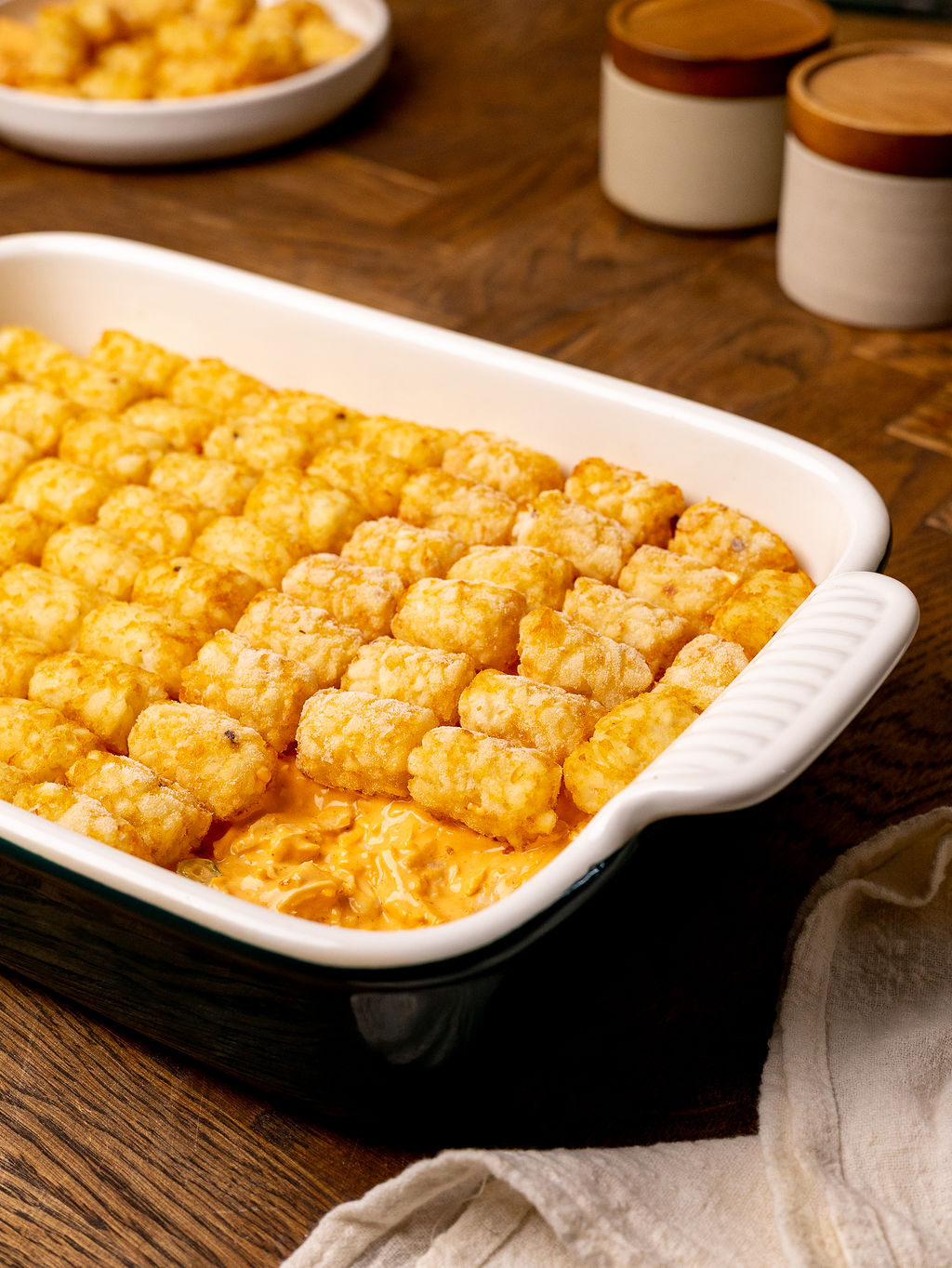 A layer of tater tots over buffalo chicken in a baking dish.