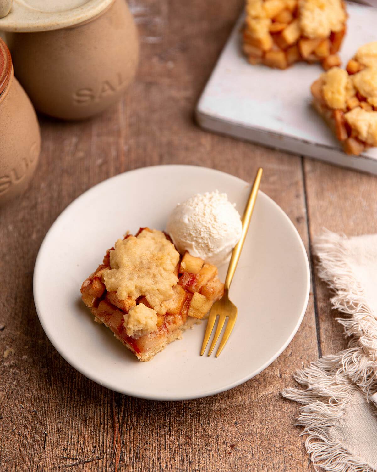 A serving of apple pie bars on a white plate with ice cream.