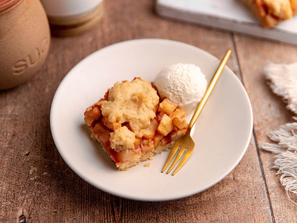 A plate with an apple pie bar serve with vanilla ice cream.