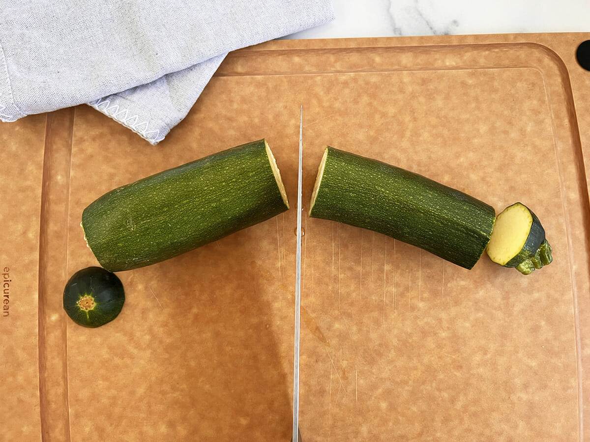 Cutting the ends off a zucchini and cutting it in half.