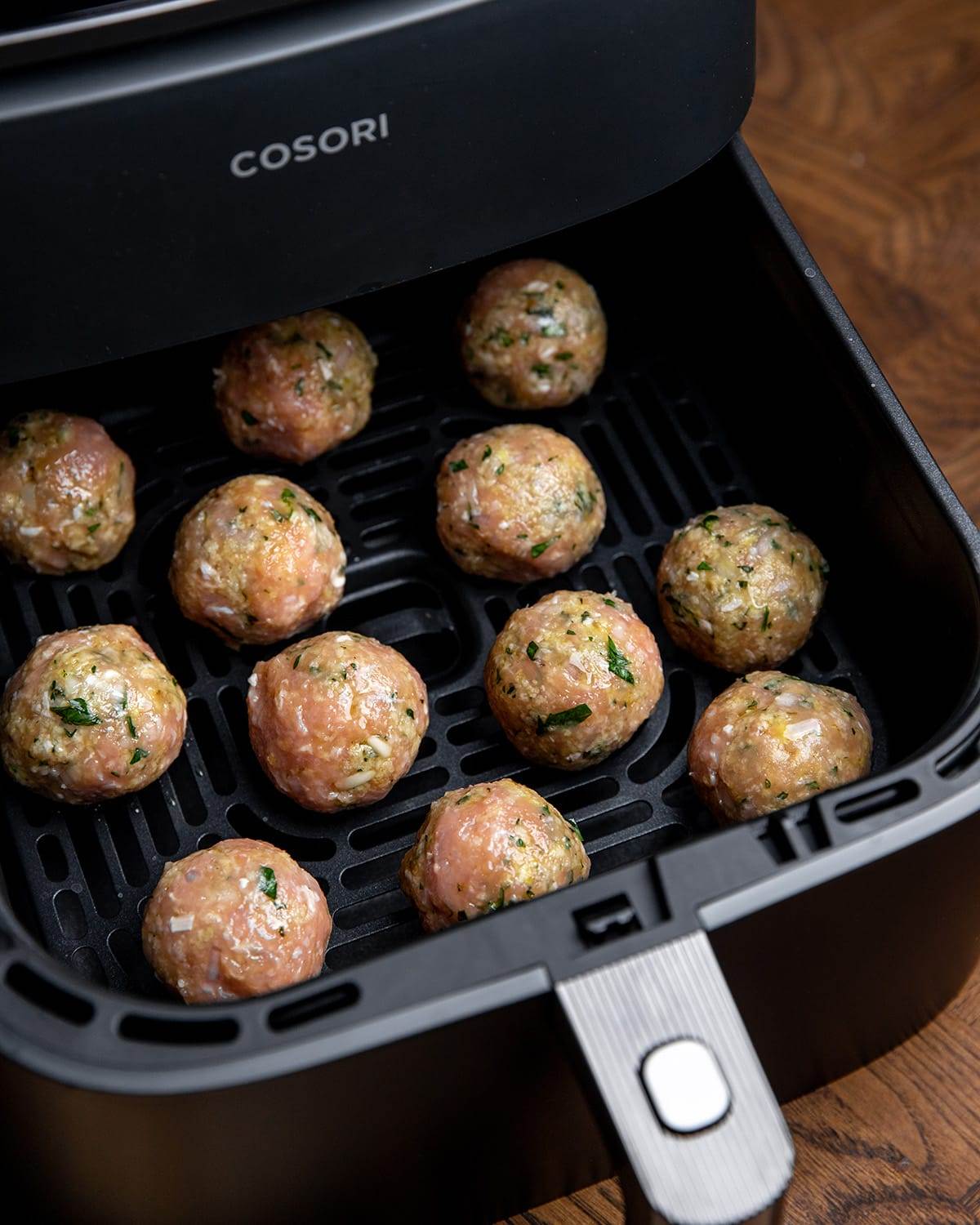Putting air fryer Greek chicken meatballs in an air fryer.