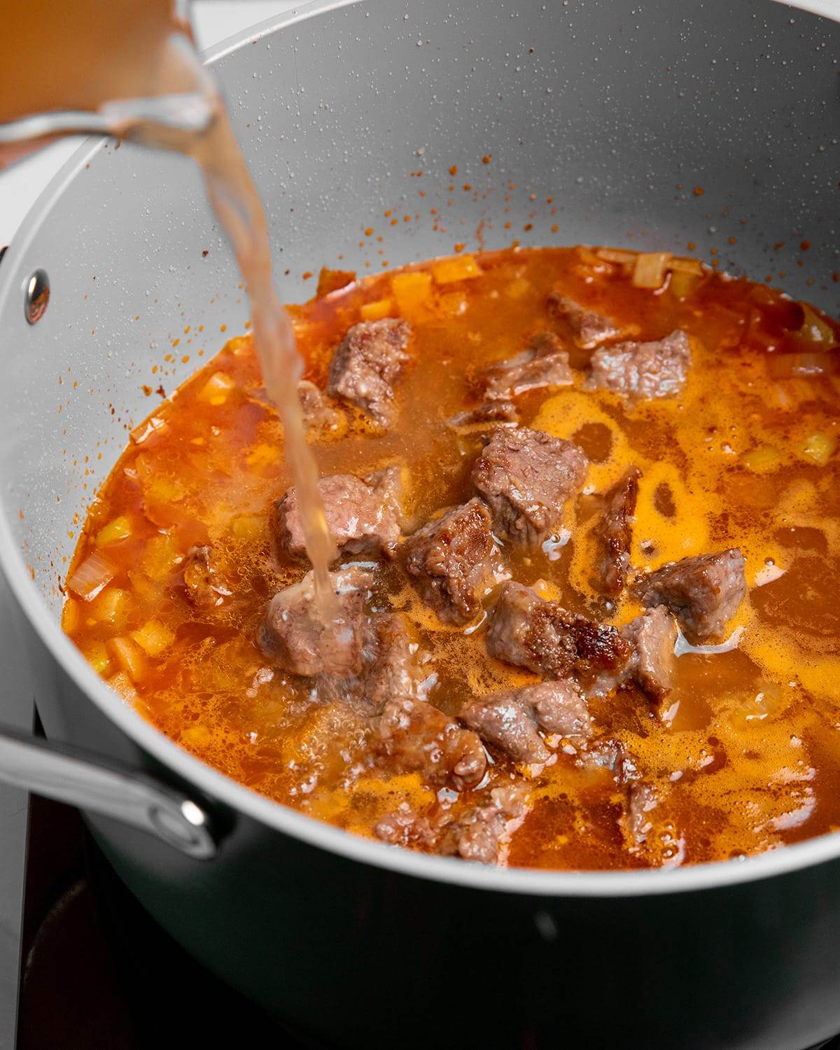 Adding broth and other ingredients to a Dutch oven for beef stew recipe.