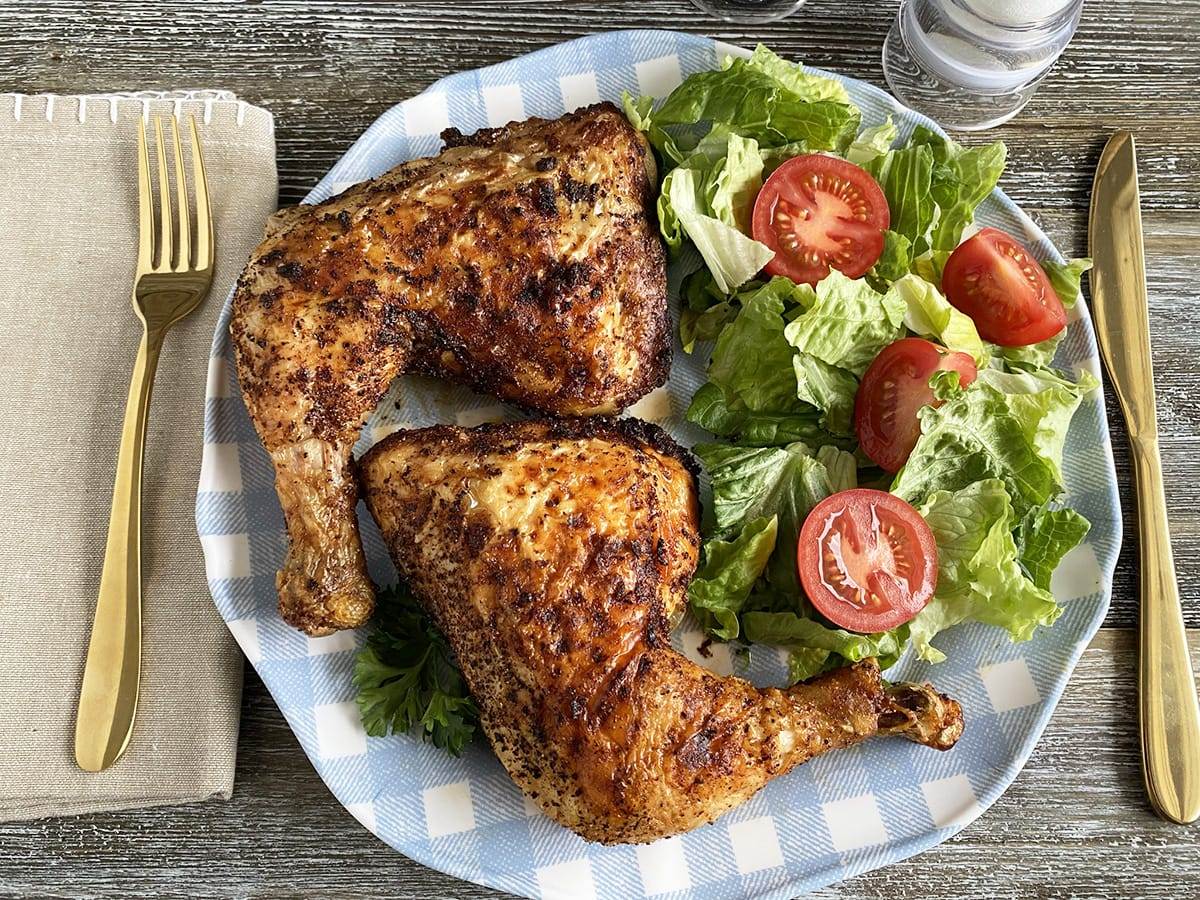 A plate of air fryer chicken leg quarters served with fresh salad.