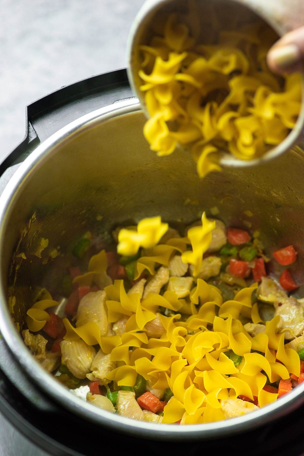 Adding the noodle to the Instant Pot to make chicken noodle soup.