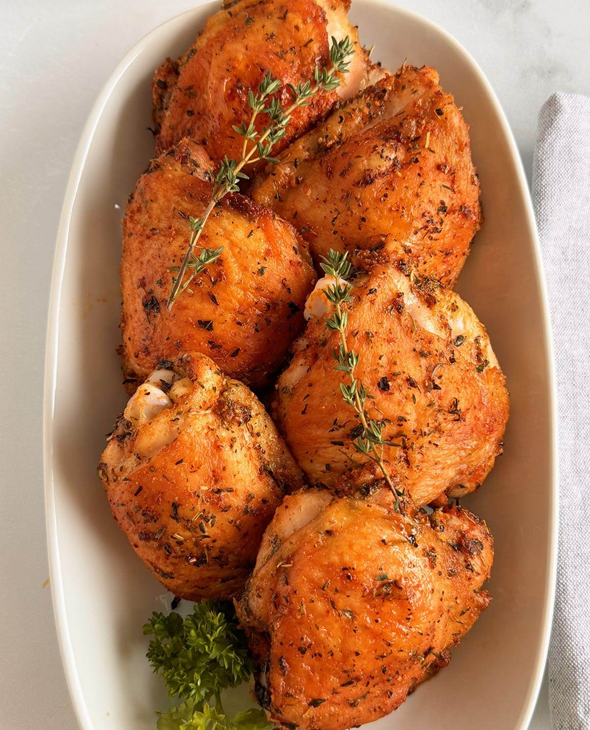 Oven baked chicken thighs served on a platter topped with fresh thyme sprigs.
