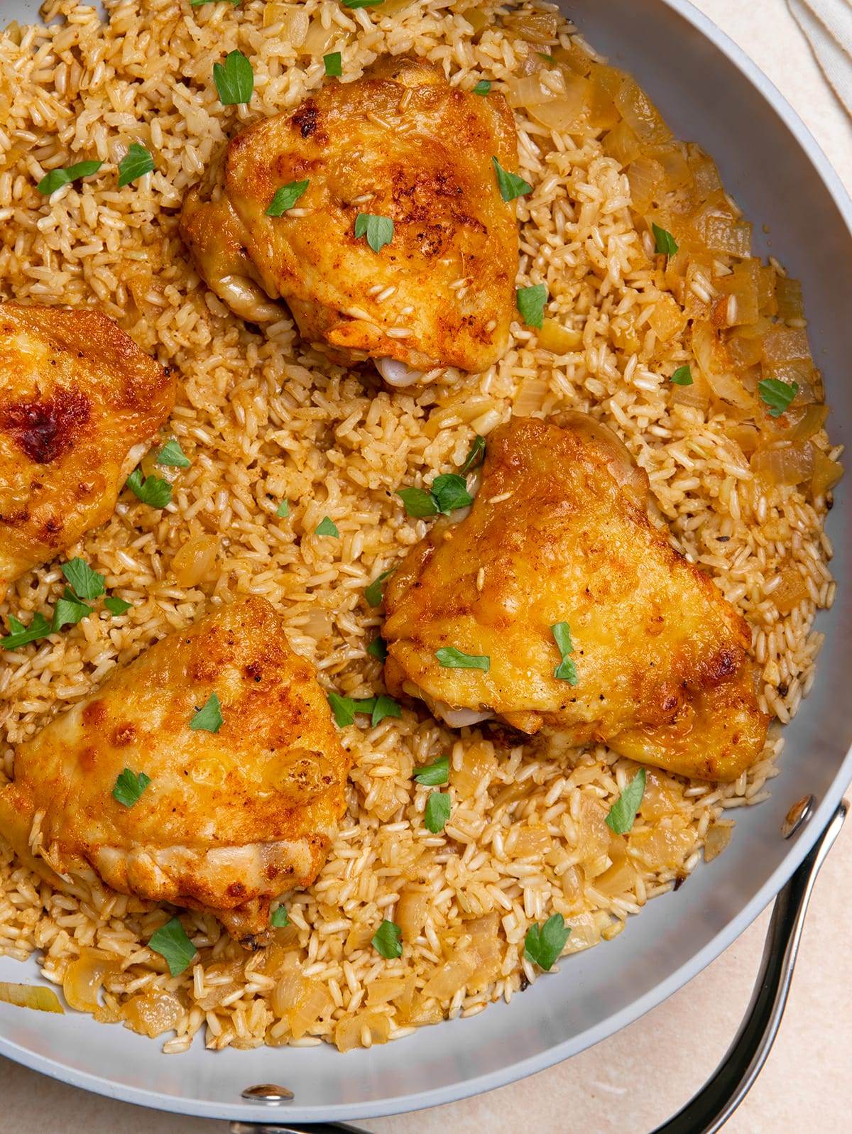 Cooked chicken thighs in a pan with brown rice, topped with fresh parsley.