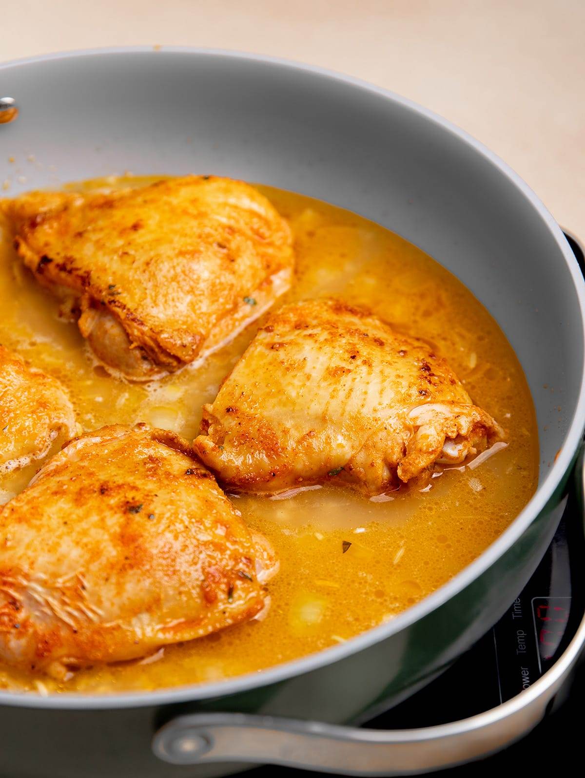 Chicken thighs cooking in a pan with brown rice.