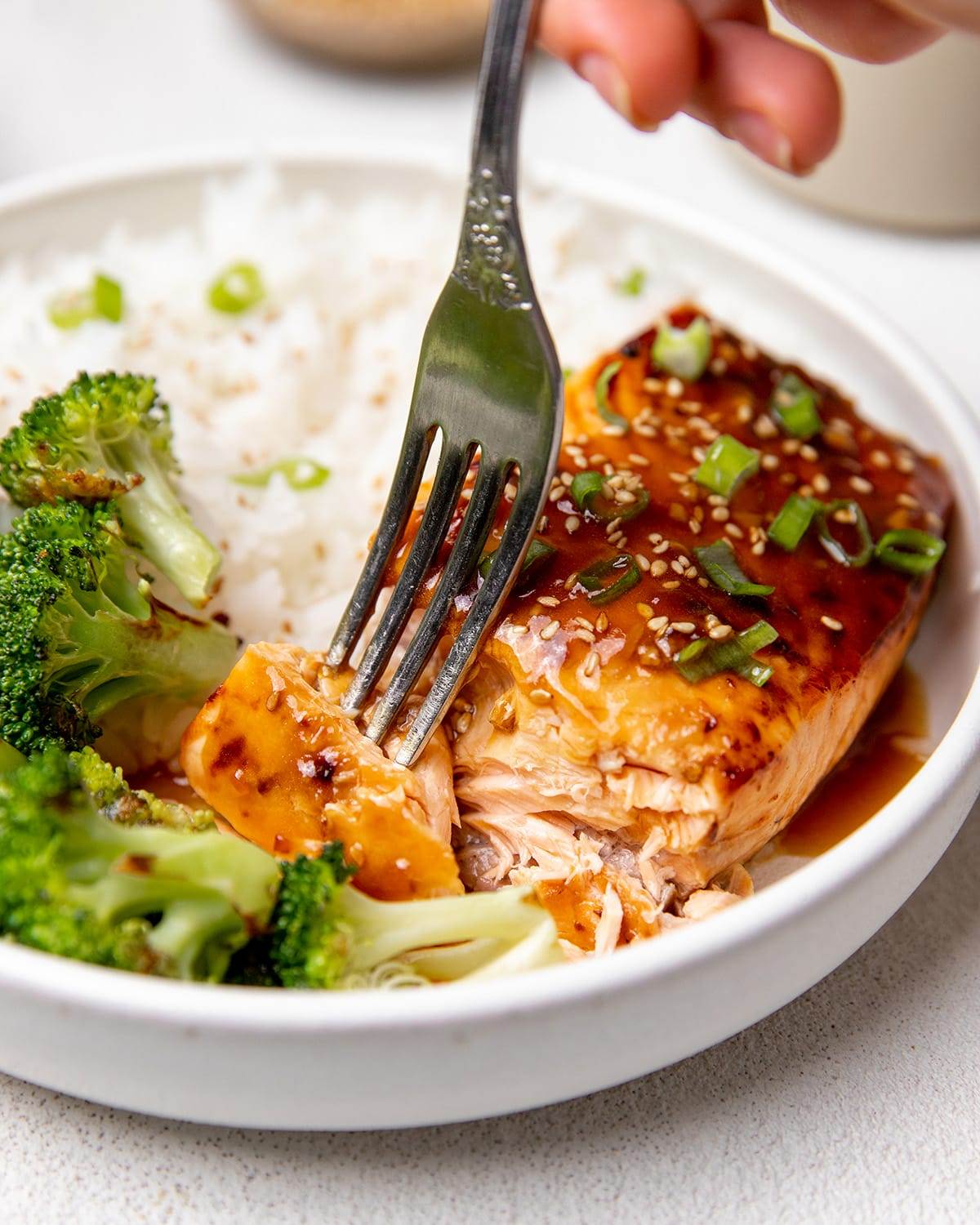 A fork with our homemade teriyaki salmon made in an air fryer and served with broccoli and rice.
