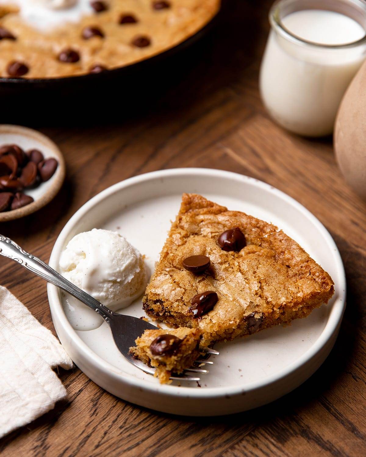 A slice of a giant chocolate chip skillet cookie on a plate with ice cream.