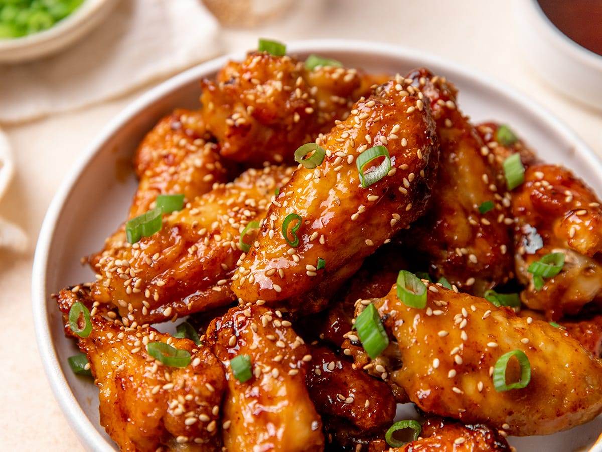 Air fryer honey garlic wings topped with sesame seeds, green onions and served in a bowl.