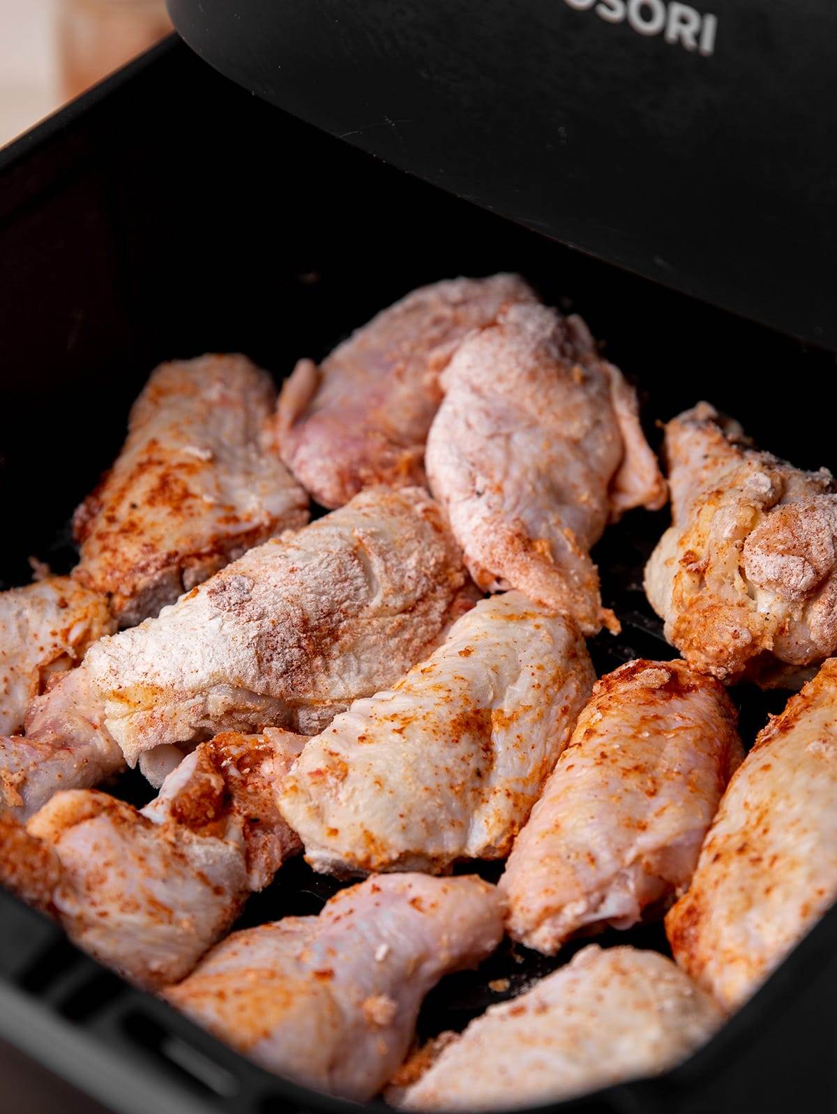 Placing seasoned chicken wings into an air fryer to be cooked.