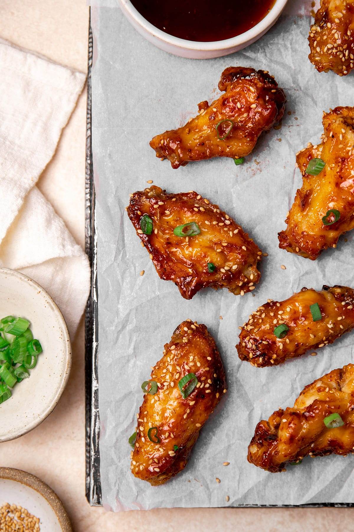Air fryer honey garlic chicken wings on a sheet pan topped with sesame seeds and green onions.