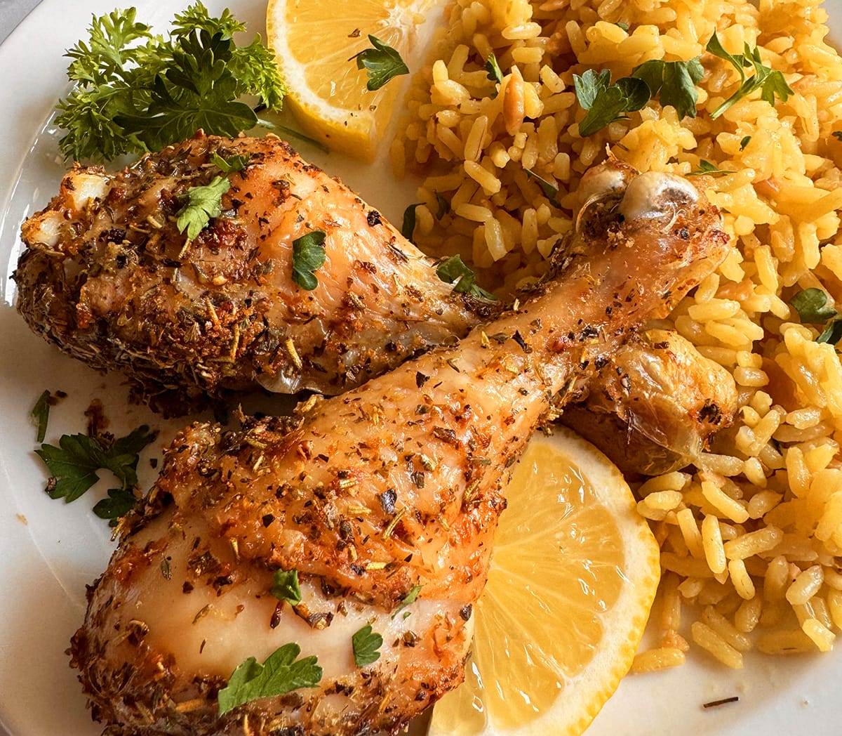 Air fryer Greek chicken legs served on a plate with rice pilaf and lemon slices. 