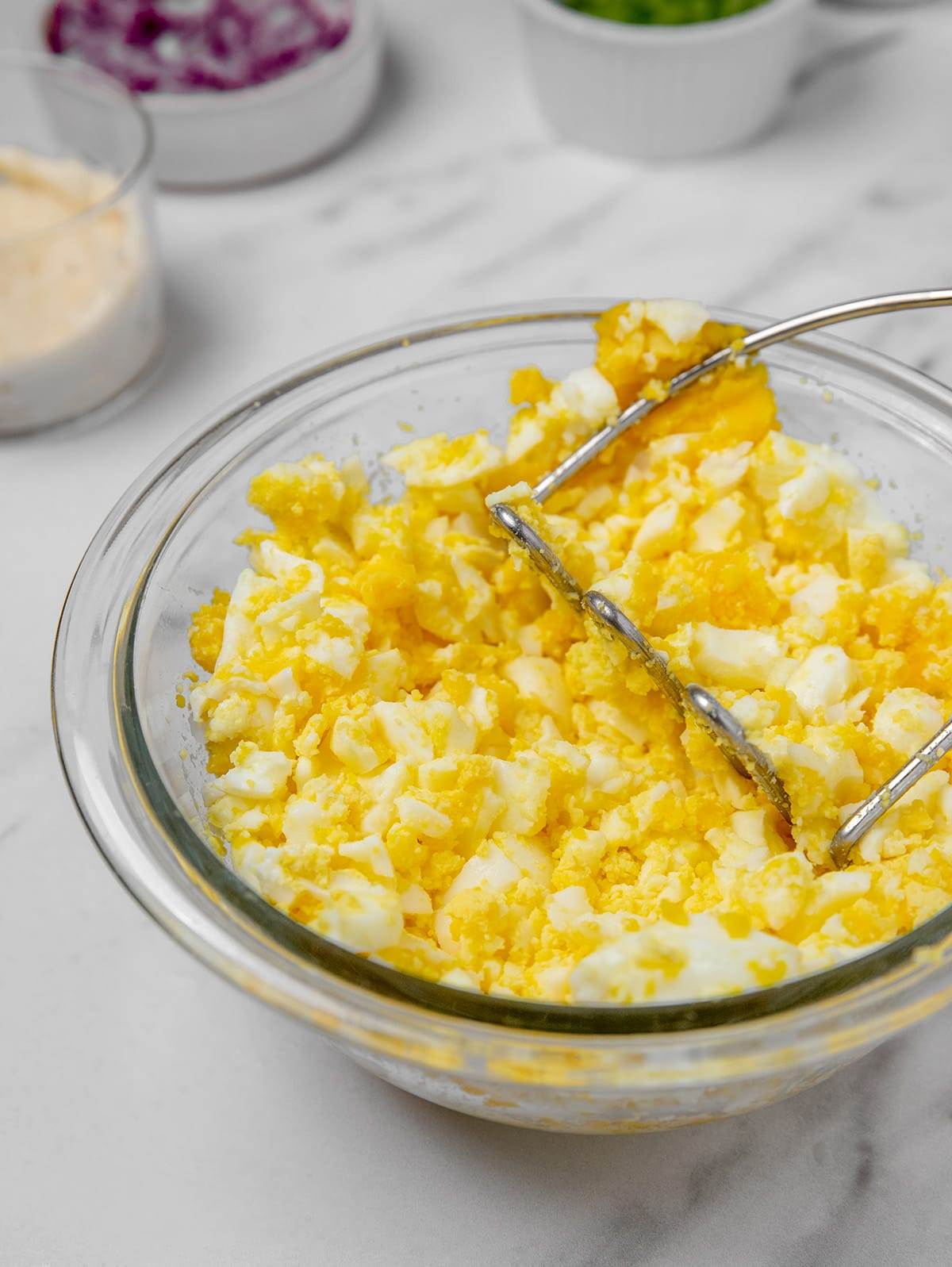 Mashing cooked eggs to make egg salad.