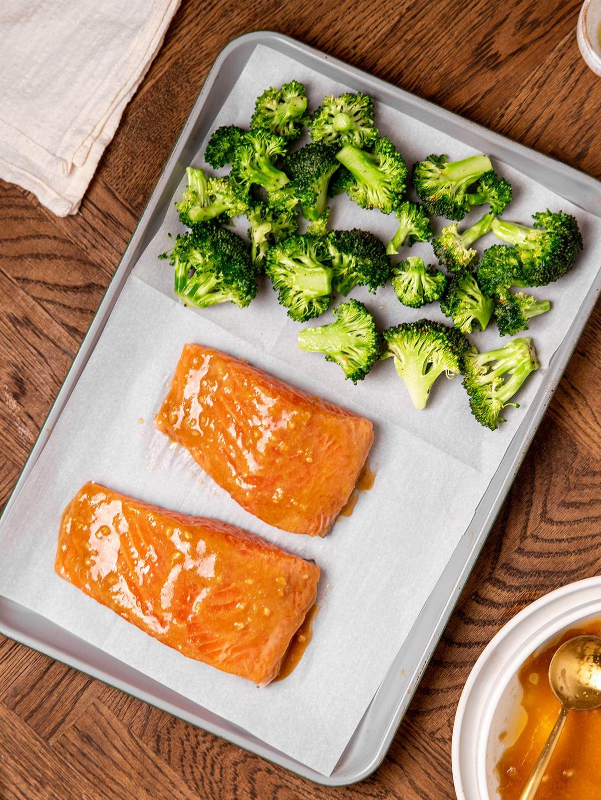 Marinated salmon filets and broccoli on a sheet pan ready to go into the oven.