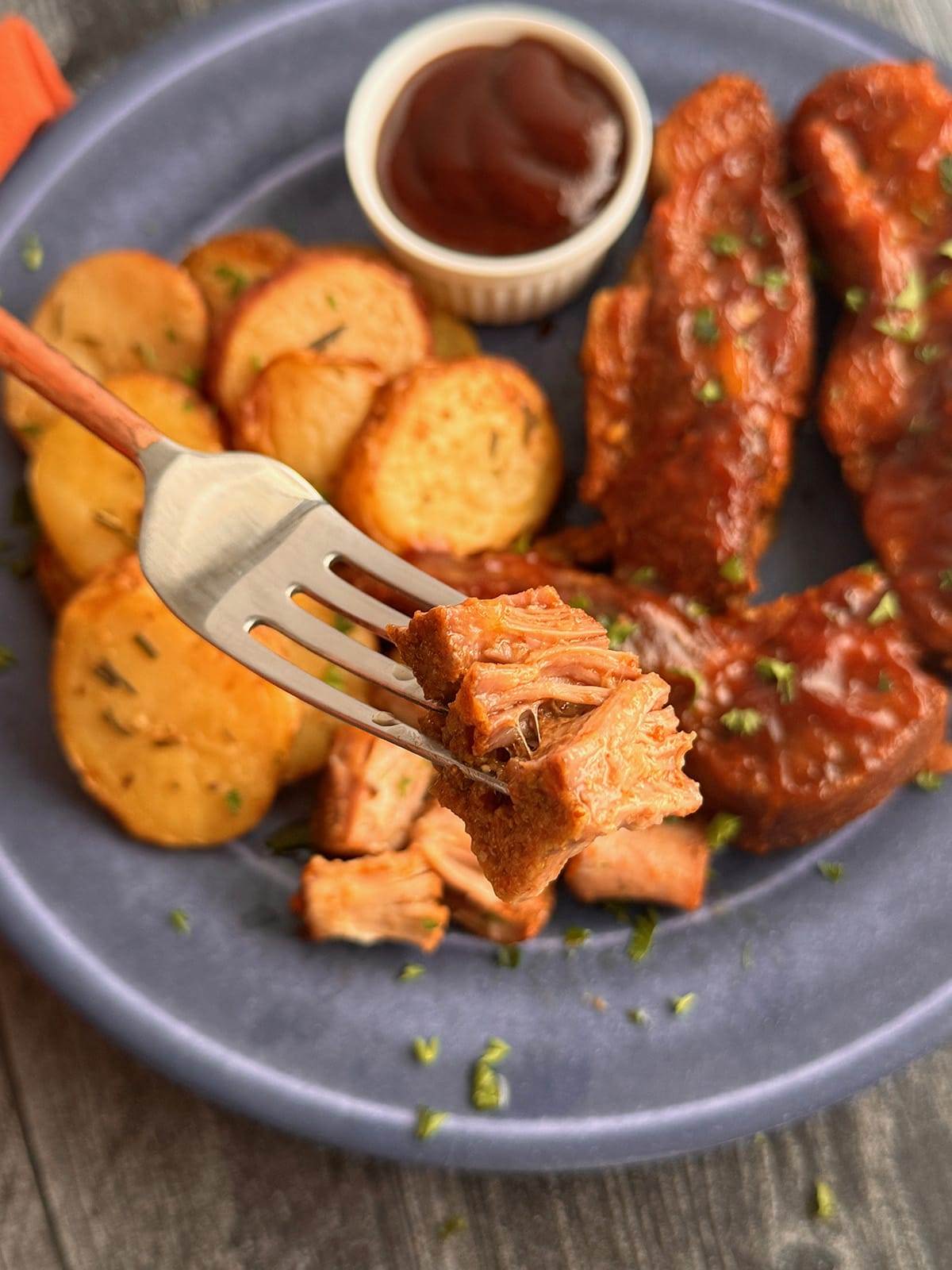 A plate with slow cooker country-style ribs and a tender piece of the meat on a fork.