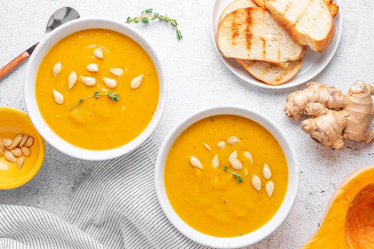 Instant Pot butternut squash and sweet potato soup served in bowls, garnished with squash seeds with a side of toasted bread.