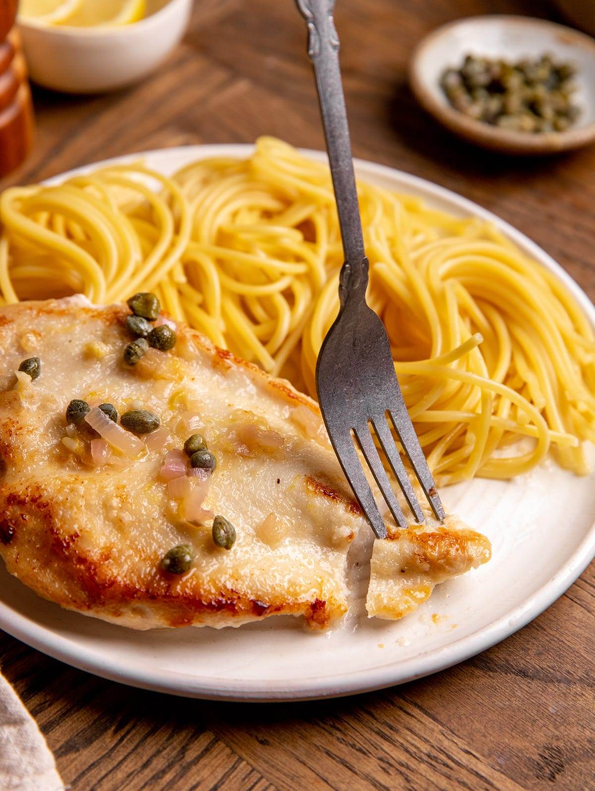 Chicken piccata served with a lemon butter sauce next to spaghetti noodles.