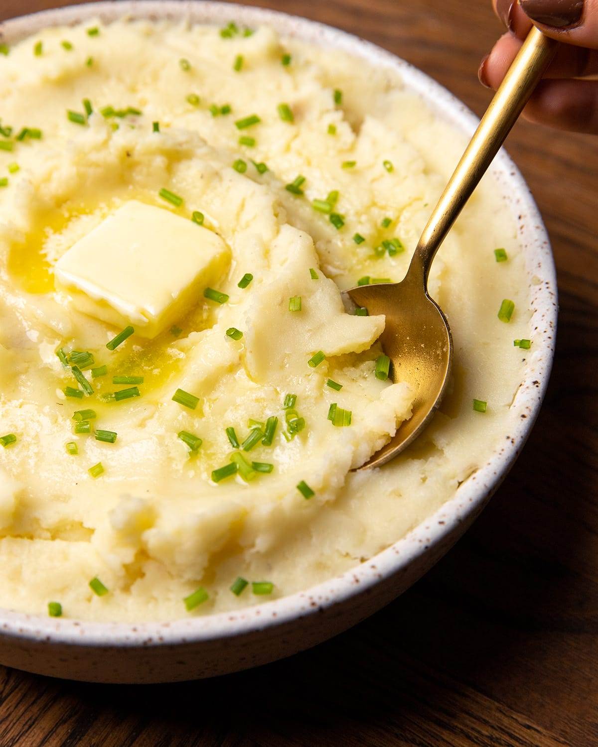 A bowl of creamy mashed potatoes with a spoon and butter.