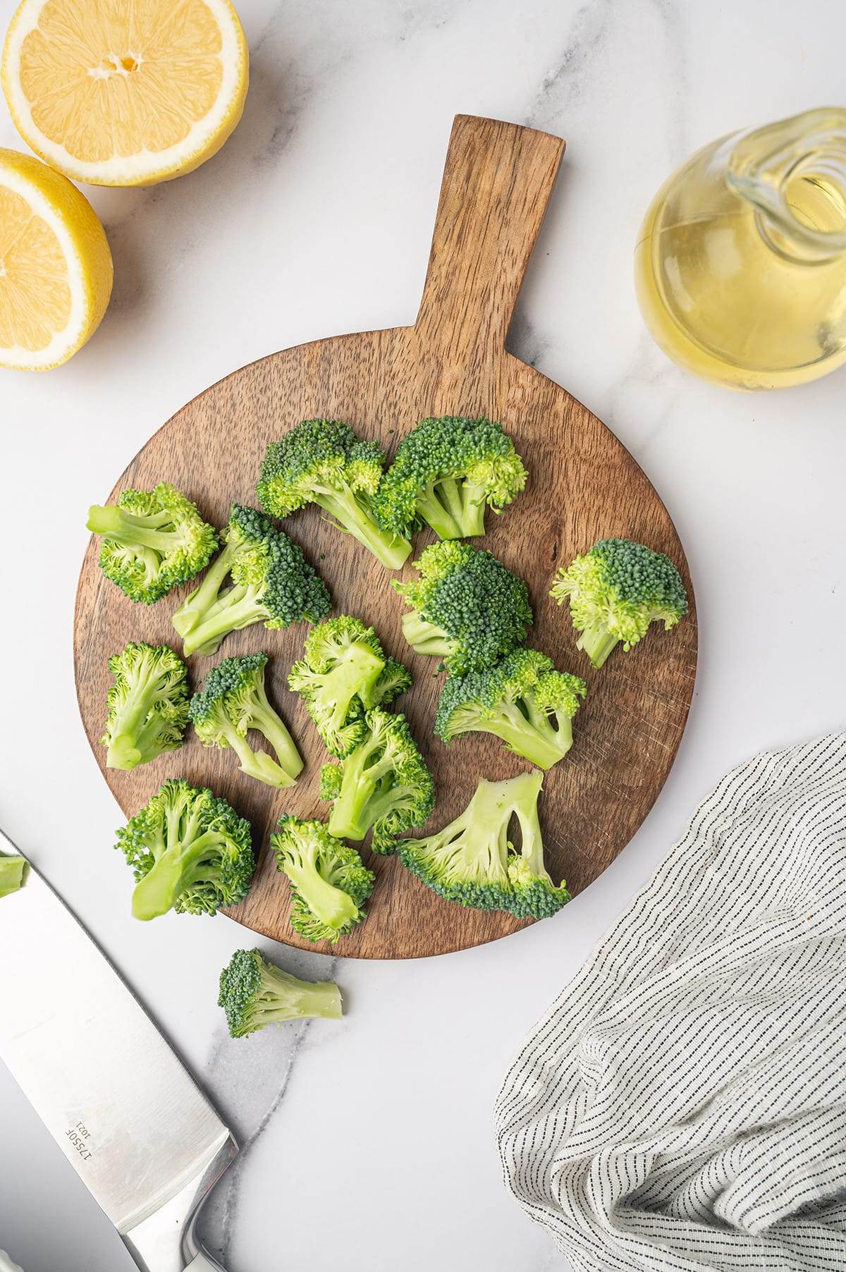 Fresh broccoli florets with lemons and olive oil on a cutting board.