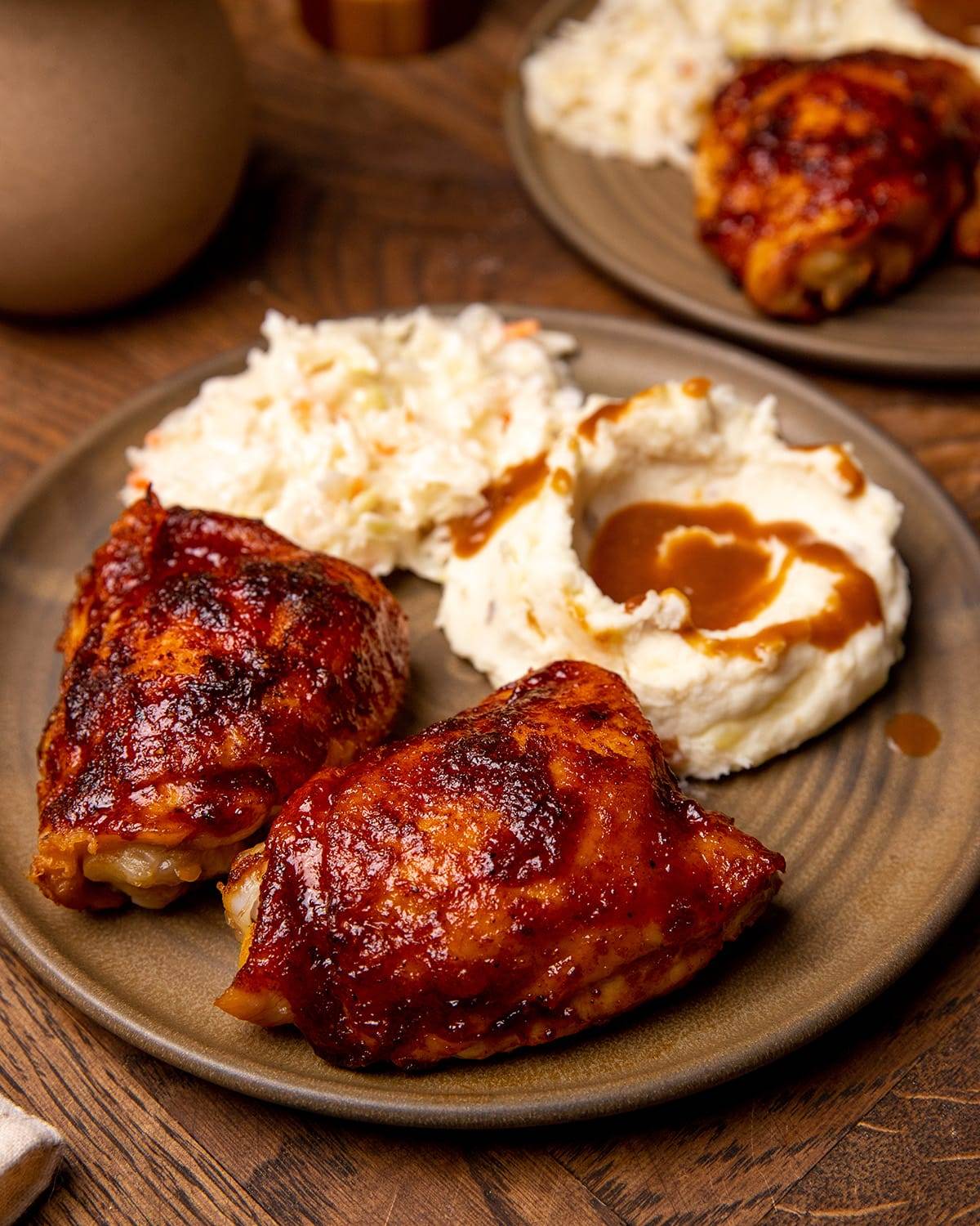 oven baked bbq chicken thighs on a plate with mashed potatoes and cole slaw.