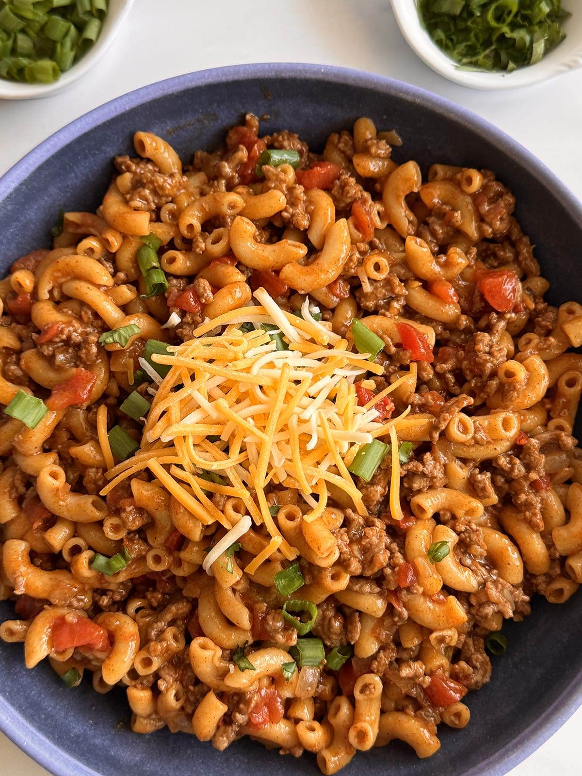 Taco pasta with ground beef in a bowl topped with shredded cheese, green onions and fresh cilantro.