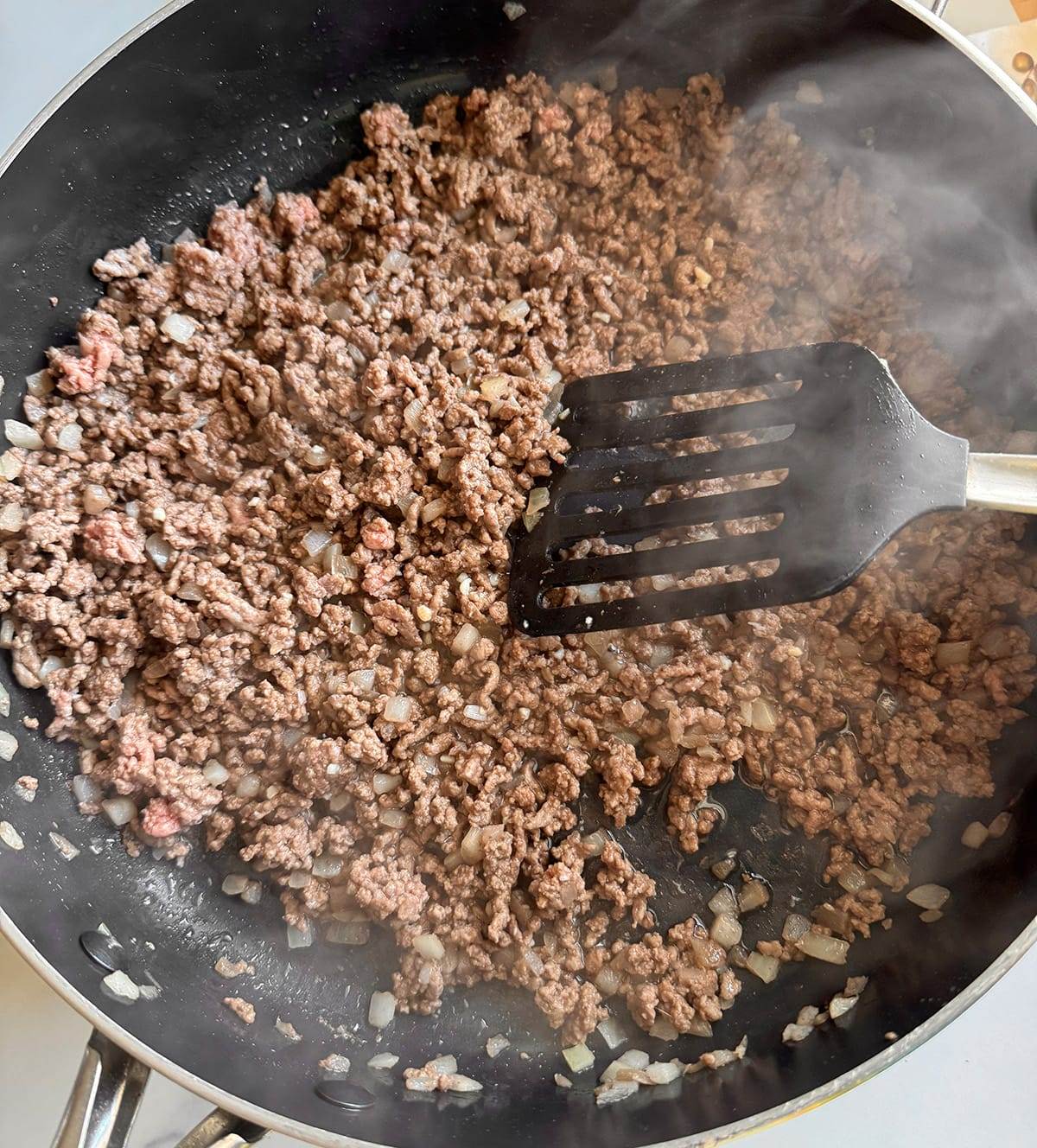 Browning ground beef and chopped onions for a taco pasta meal.